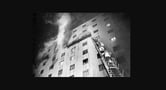 Firefighters climb a ladder into a burning building.