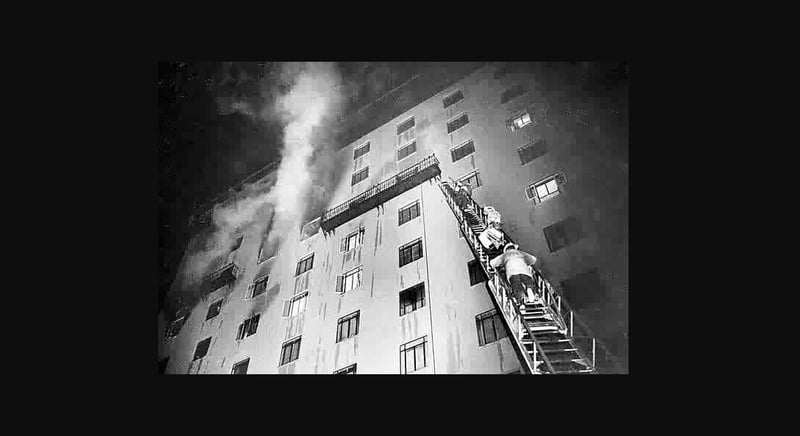 Firefighters climb a ladder into a burning building.