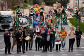 More than a dozen people play a variety of instruments or carrying structures with puppets on top walk through a street during the Purim parade.