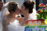 Two women in bridal gowns kiss.