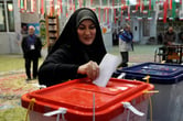 A woman in a headscarf puts a ballot in a plastic bin.