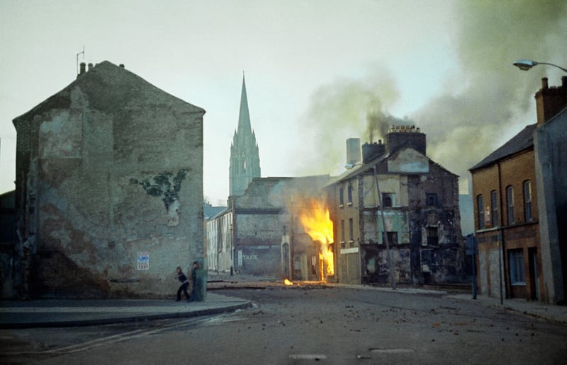 A building burns as two people stand behind another building in Northern Ireland in the aftermath of Bloody Sunday.
