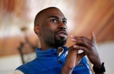 Wearing a blue vest, DeRay Mckeesson gestures with his hands while speaking.