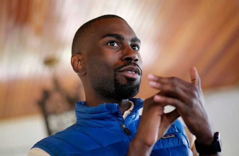 Wearing a blue vest, DeRay Mckeesson gestures with his hands while speaking.