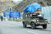 A rusting vehicle piled high crosses a border.