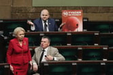 One lawmaker stands while two sit near a poster poster showing an artistic graphic of a fetus in the Polish Parliament.