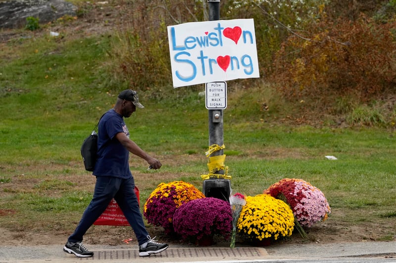 A man walks past a sign on a street post that reads "Lewiston Strong"