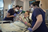 A woman in a hospital room uses a smartphone while medical personnel look at the screen.