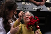 A woman supports an elderly woman holding carnations.