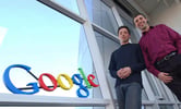 Sergey Brin and Larry Page pose for a photo next to a Google sign inside the company headquarters.