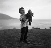 A young boy holding a big fish on a beach.