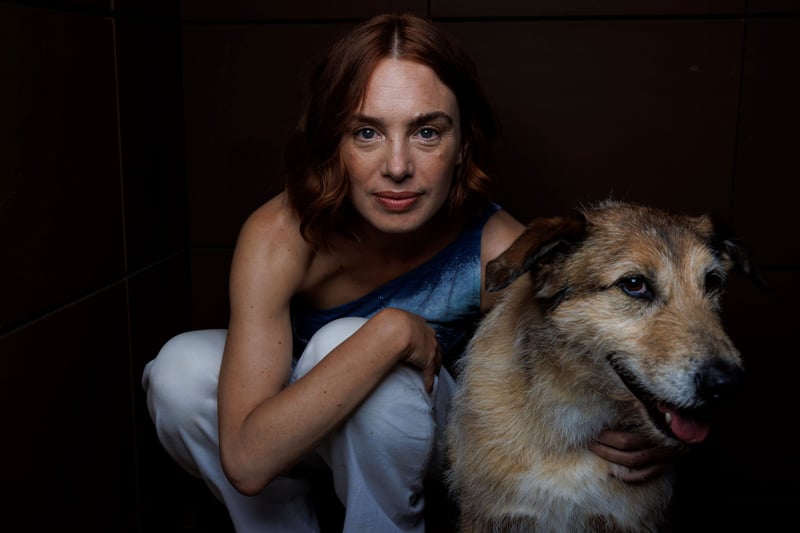 A woman poses crouching next to a dog.