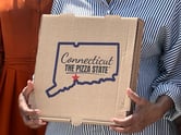 a woman holds a pizza box with the phrase "connecticut the pizza state" on it