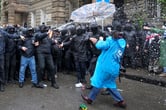 A woman in a blue raincoat blocks police spray with an umbrella.