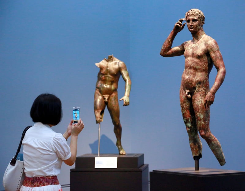 A woman takes a photo of a statue of a man.