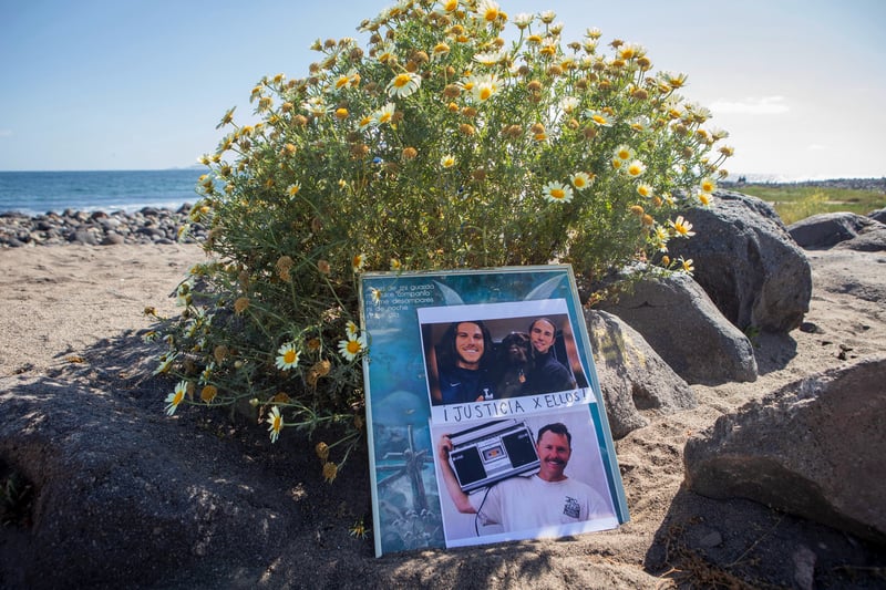 Pictures of Jack Carter Rhoad and Jake and Callum Robinson on a poster that's leaning against a small bush on a Mexican beach.