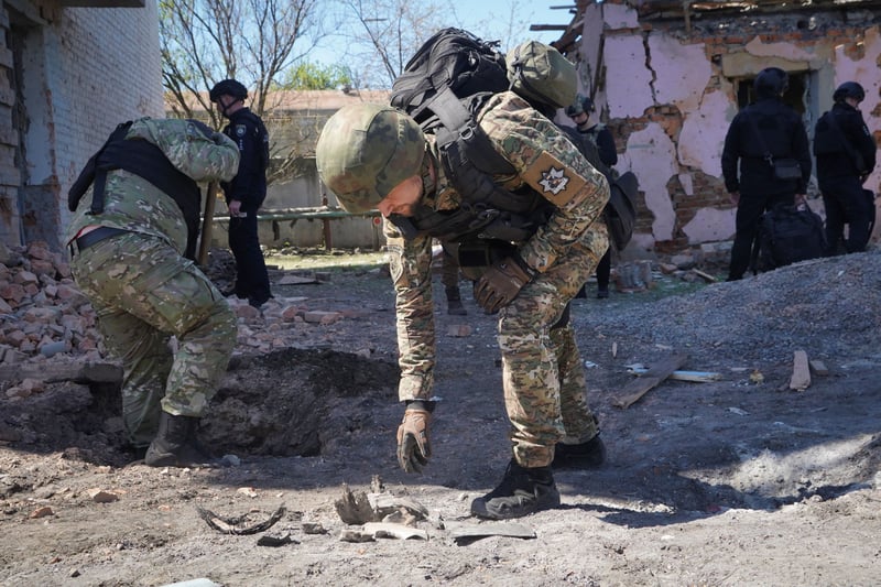 A man in fatigues and a helmet picks up fragments from the ground.