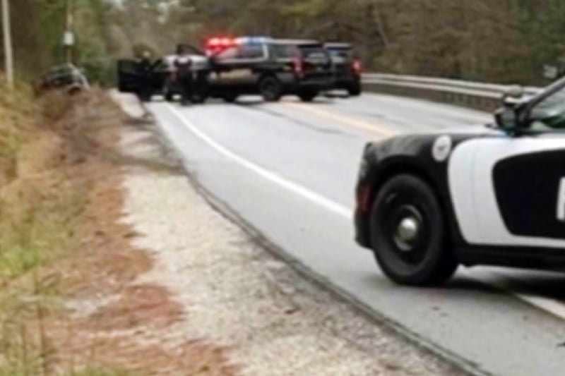 An image taken from video showing several police vehicles stopped on single-lane road, with a vehicle seemingly crashed into a pole.