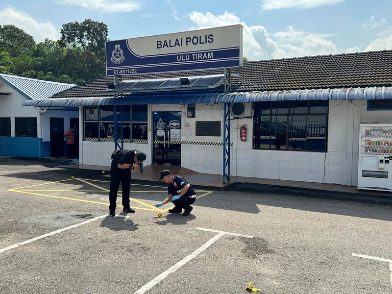 Two Malaysian police officers examine the scene of a shooting outside a police station.