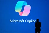Satya Nadella stands in front of a large screen displaying the logo for Microsoft Copilot