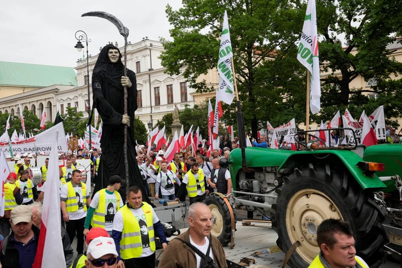 Protesters marching with a tractor, flags and a Grim Reaper figure.
