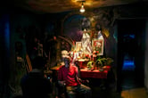 A man sitting in a chair next to an altar adorned with Santeria and Catholic deities, along with a photo of Fidel Castro.