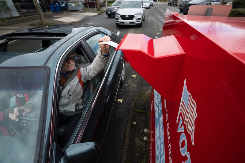 A person drops off a vote-by-mail ballot while in their car.