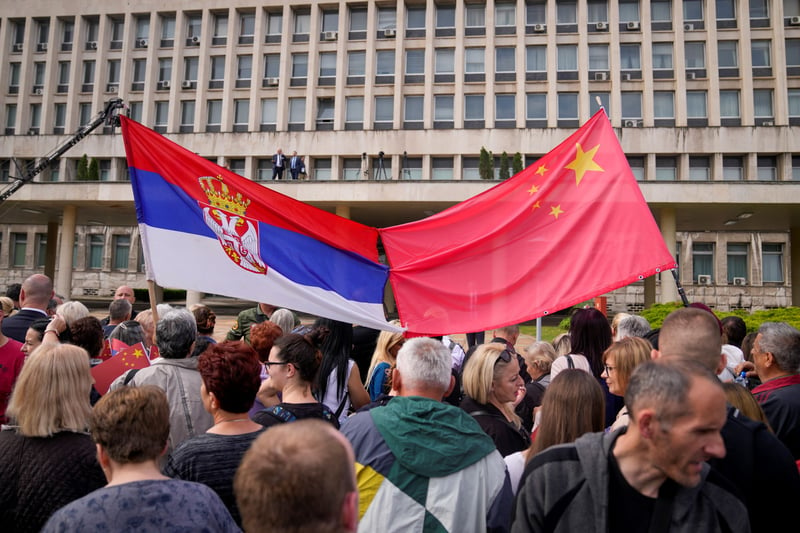 Members of a crowd hold a Serbian and a Chinese flag.
