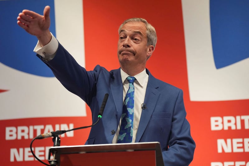Nigel Farage raises his hand at a podium.