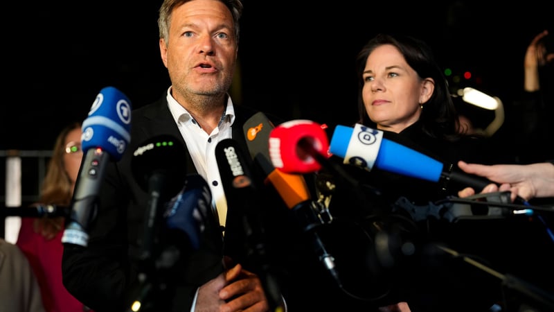 Robert Habeck speaks into microphones held toward him as Annalena Baerbock stands beside him.