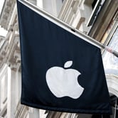 A black flag with a white Apple logo on a horizontal pole attached to a building's facade in England.