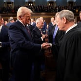 Donald Trump shakes John Roberts' hand as they are surrounded by members of Congress and others.