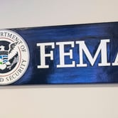 A blue sign with FEMA in white on the right and a Department of Homeland Security seal on the left