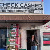 A woman in a black and brown hoodie and blue jeans stands outside of a business with a white sign that reads in black letters "check cashed."