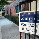 A "Vote Here" sign outside of a brick building