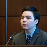 A man wearing a suit and sitting on the stand in a courtroom