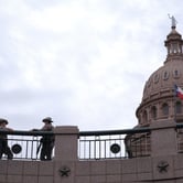 The top of the Texas Capitol building in the background with two state police officers standing off to the side.