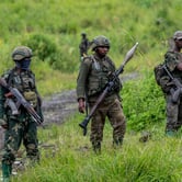 Three M23 rebels in military gear, holding weapons, stand alert in a grassy area in Kibumba, eastern Democratic Republic of Congo.