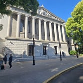The California Supreme Court building in Sacramento, California, featuring tall white columns and classical architectural details with people standing outside.