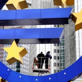 Workers on a lift inspect a large blue euro symbol with yellow stars.