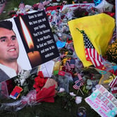 A memorial with flowers, flags, and a photo honors a deceased man.