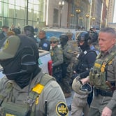 U.S. Border Patrol Cmdr. Greg Bovino walks surrounded by fellow Border Patrol and federal law enforcement officers, some wearing tactical gear, near a white truck outside the Dirksen Federal Courthouse.