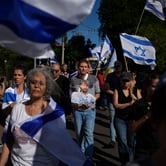 A small group of people walk with Israeli flags. One holds a cutout photo of a blond, bearded man.