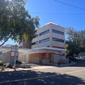 A white three-story building surrounded by a gate and boarded up entrance.