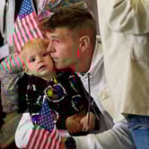 A kneeling man wraps his arm around a young child holding a small U.S. flag.