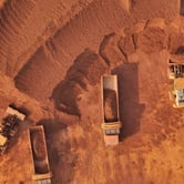 Two trucks and two diggers full of rust-colored earth in an overhead view.
