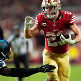 San Francisco 49ers running back Christian McCaffrey carries the football while running past a diving Carolina Panthers defender during a game.
