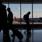 Four silhouetted people with luggage walk past plate glass windows with Southwest planes on the tarmac.