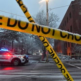 Police car behind crime-scene tape on snowy street.