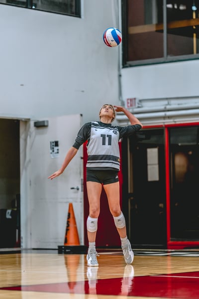 A player in a gray and white jersey reaches overhead for the ball.